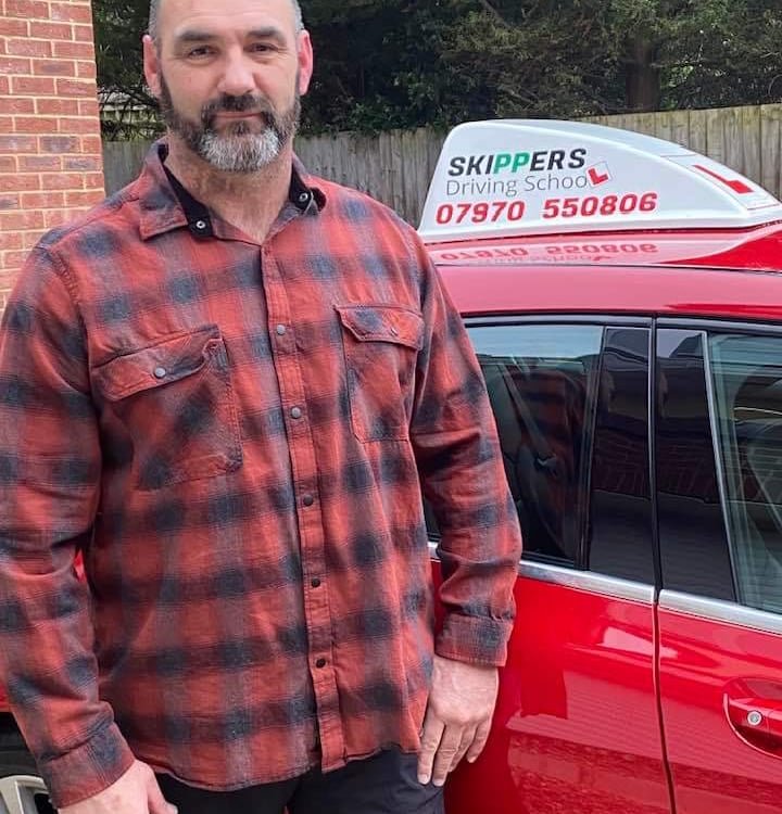 Manfred from Skippers Driving School next to his red tuition car in Chippenham, Wiltshire